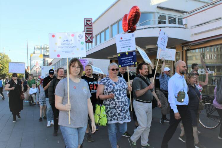 Ihmiset marssivat kulkueena Helsingin keskustassa ja pitävät mukanaan mielenosoituskylttejä.